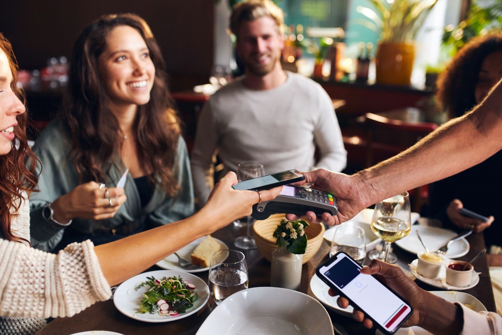 Guests at a restaurant paying with smartphones while enjoying a meal, symbolizing seamless Wi-Fi connectivity and LongFi-powered monetization.