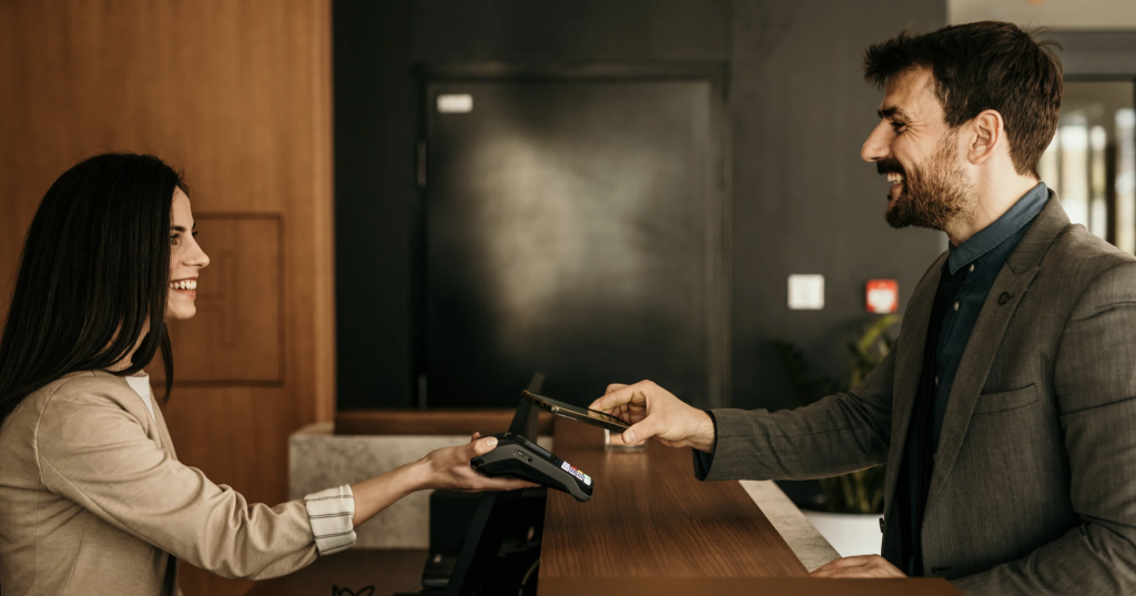 Hotel receptionist and guest completing mobile payment at front desk counter